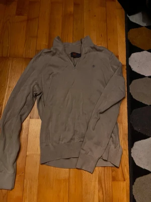 Beige halvziptröja från Morris - Snygg beige långärmad tröja från Morris med halvzip och liten broderad logga på bröstet. Tröjan har ribbade muddar vid ärmslut och nederkant, perfekt för en stilren och avslappnad look. Perfekt att ha över skjorta eller vanligt för en stilren look😃🥶.