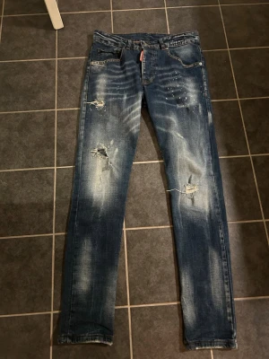 Dsquared2 Jeans - Extremt snygga jeans från märket Dsquared2 med slitningar som design. Nypris är ca 4500 och de har bra passform (slim ungefär, inte skinny). Passar de som är mellan 170-185cm skulle jag säga och mellan 55-70kg beror på person till person. Pris är ej hugget i sten, mvh. 