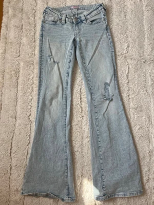 Trendiga ljusblå low waist bootcut jeans - Säljer ett par ljusblå low waist bootcut jeans från Gina Tricot🩵🩵jeansen har egengjorda hål på benen och fina detaljer på fickorna!! Byxorna har varit vikta därav viksträcken på benen. 
