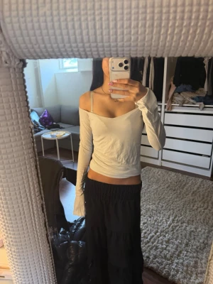 Vit långärmad omlottopp - Trendig vit långärmad topp med omlottkänsla och v-ringad hals. Sitter offshoulder och har en slim passform som framhäver figuren. Perfekt att styla med kjol eller jeans för en snygg look.