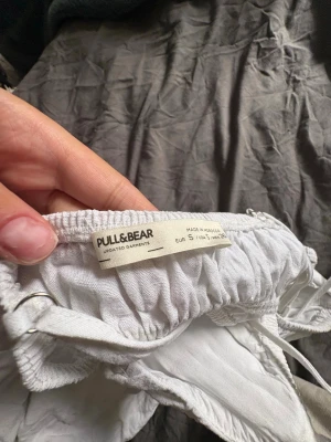 Vit sommarklänning från Pull&Bear - Söt vit kortklänning från Pull&Bear med smala axelband och resår i midjan. Tillverkad i ett lätt och luftigt material, perfekt för varma dagar. Enkel och stilren design som passar till många tillfällen.