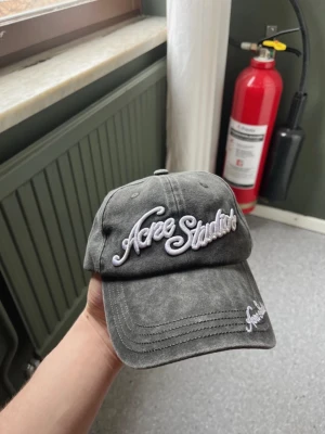 Acne Studios keps - Säljer en grå keps från Acne Studios med vit broderad logga framtill och på skärmen. Kepsen har en klassisk böjd skärm och justerbar rem bak. Tillverkad i bomull med tvättad look för en avslappnad vibe. Använd ett fåtal gånger! Som helt ny.