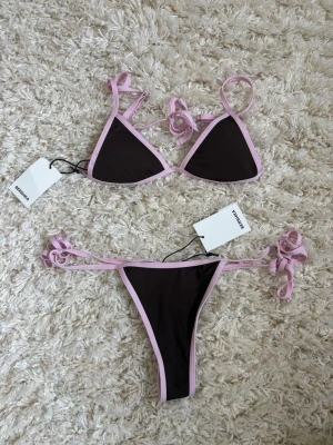 Bershka brun bikini med rosa kanter  - Jättefin bikini från Bershka i brun med ljusrosa kanter. Både överdel och underdel har smala band som knyts, vilket ger en snygg och justerbar passform🙌 Överdelen är i storlek S och underdelen är i storlek M! 💗Helt nyköpt och aldrig använda.  Perfekt för sommardagar på stranden eller vid poolen.