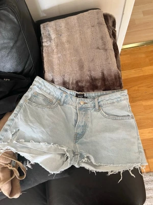 Ljusblå denimshorts med fransig kant - Säljer ett par ljusblå denimshorts från 157 med fransig och rå kant nertill. Klassisk femficksmodell med knappar framtill. Perfekta för sommaren och ger en avslappnad vibe.