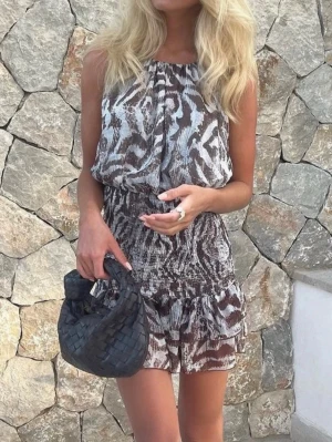  Ny trendig Brun och vit zebra klänning från Zara - Säljer en kort klänning från Zara med zebramönster i bruna och vita toner. Klänningen är ärmlös, har smockad midja och volang nertill. Perfekt för dig som gillar djurmönster och vill ha något snyggt och bekvämt.