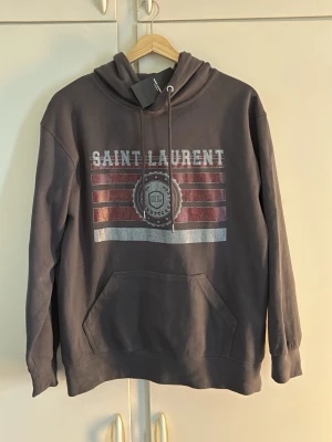 YSL Saint Laurent Hoodie S - Helt ny YSL Saint Laurent hoodie i storlek S till superpris! En mycket fin grå färg ihop med vita och vinröda detaljer. Helt oanvänd! Hoodien är 1 till 1. Hör gärna av er vid frågor eller funderingar!😁