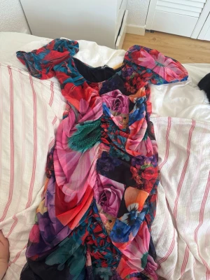 Färgstark blommig klänning Desigual - Säljer en kort klänning från Desigual med färgstarkt blommigt mönster i rosa, rött, blått och lila. Klänningen har puffiga korta ärmar och är tillverkad i ett lätt syntetmaterial. Perfekt för dig som gillar att sticka ut med din stil! Kan ksk gå ner lite i pris