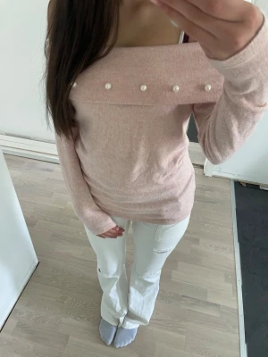 Rosa off shoulder tröja med pärlor - Snygg ljusrosa off shoulder tröja med dekorativa pärlor längs kragen. Tröjan har långa ärmar och är tillverkad i ett mjukt stickat material som känns skönt mot huden. Perfekt för dig som gillar en feminin och trendig look.