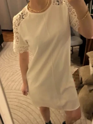 Studentklänning❤️ - Snygg vit kortklänning med rund halsringning och korta ärmar i vacker spets. Klänningen har en rak passform och är perfekt för dig som gillar en stilren look med fina detaljer. Materialet känns lätt och luftigt.