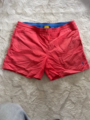  badbyxor från Polo Ralph Lauren M - Snygga rosa badbyxor från Polo Ralph Lauren med elastisk midja och sidofickor. Klassisk logga broderad i blått på framsidan. Materialet är lätt och snabbtorkande, perfekt för strand eller pool. Bakficka med lock och ventilationshål. Välanvända men har mer att ge.