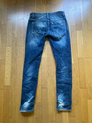 Blå dondup jeans med slitningar  - Snygga blå slim fit jeans med slitningar och tvättade detaljer på knän och bakfickor. Klassisk femficksmodell med kontrastsömmar och låg midja. Perfekta för en avslappnad och trendig look.