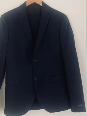 Mörkblå kostym från Premium, skvaj st 44 och byxor trl 46 - Snygg mörkblå kavaj från Premium by Jack & Jones . Klassisk modell med två knappar, smala slag och fickor med lock. Perfekt för en stilren look och passar till både skjorta och t-shirt. Materialet känns mjukt och följsamt.