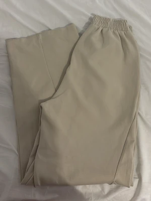 Beige mjukisbyxor med resårmidja från Zara  - Snygga beige mjukisbyxor med avslappnad passform och resår i midjan. Byxorna har raka ben och sidofickor, perfekta för en chill och bekväm stil. Tillverkade i mjukt material som känns skönt mot huden.