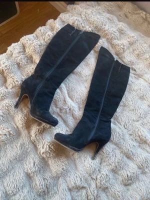 Svarta höga stövlar med klack - Snygga svarta knähöga stövlar med smal klack och dragkedja på sidan. Tillverkade i mockaliknande material och har en elegant, smal siluett. Perfekta för att lyfta vilken outfit som helst. Storleken är 39 men skulle säga 38,5 för de är lite mindre i storleken. Lite smuts men går att tvätta. 