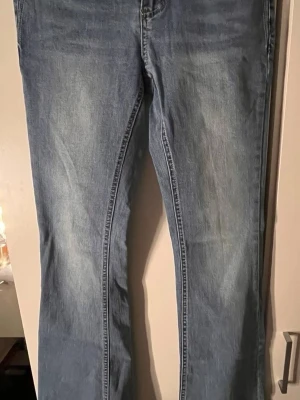 Ljusblå bootcut jeans med broderi - Säljer ett par ljusblå bootcut jeans med snygga broderade detaljer på bakfickorna. Jeansen har klassisk femficksdesign och är tillverkade i mjukt denimtyg. Perfekta för dig som gillar en avslappnad men ändå trendig stil.