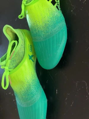 Neongröna Adidas fotbollsskor. Slutat säljas! - Säljer ett par riktigt snygga Adidas fotbollsskor i neonlime och turkos. Skorna har snörning, textilfoder och en ovandel i syntetmaterial med NSG-teknologi för bättre bollkontroll. Perfekta för dig som vill sticka ut på planen och maxa din speed.slutat säljas. Pris kan diskuteras!