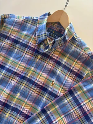 Ralph Lauren Oxford stretch skjorta - Säljer en klassisk rutig skjorta från Ralph Lauren i blå, vit, gul, grön och rosa. Skjortan har lång ärm, knappar framtill och ikonisk broderad logga på bröstet. Perfekt för dig som gillar färg och stil! Materialet är mjuk bomull.