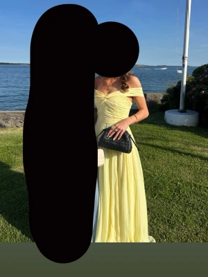 Ljusgul balklänning  - Superfin ljusgul bal klänning med offshoulder och draperad överdel från by Malina.  Tillverkad i ett lätt och luftigt material som ger ett elegant fall. Lite fläckig längst ner