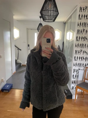 Mörkgrå teddyjacka med dragkedja - Mysig mörkgrå teddyjacka med dragkedja framtill och hög krage. Jackan har en fluffig,mjuk o håller värmen under sommarkvällarna✨ Jackan har också en rak passform. OPS! Fickorna är lite sönder vilket gör att de inte är pålitliga till förvaringssyfte!!!! Utöver detta är den perfekt💓