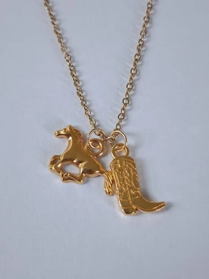 Guldigt halsband med häst och cowboyboot - Snyggt halsband i guldfärgad rostfritt metall med två berlocker: en springande häst och en detaljerad cowboyboot. Perfekt accessoar för dig som gillar westernstil och unika smycken. Kedjan är tunn och smidig, och berlockerna har en cool, ungdomlig vibe.