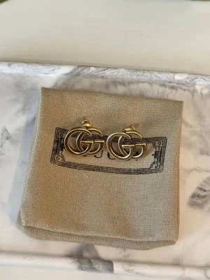 Gucci GG örhängen i guldton - Snygga örhängen från Gucci i klassisk GG-design. Örhängena är i guldtonad metall och har en stilren, rundad form som ger en lyxig känsla. Perfekta för dig som vill ha en ikonisk accessoar med exklusiv känsla.