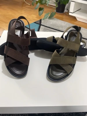 Chunky sandaler i brunt och olivgrönt - Snygga sandaler med breda remmar i brunt och olivgrönt. Modellen har en chunky sula och öppen tå, samt justerbar hälrem. Perfekta för en trendig och avslappnad look. Tillverkade i syntetmaterial med mockakänsla.helt ny