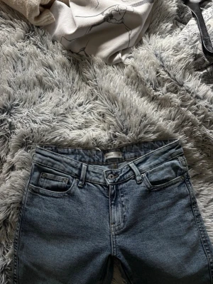 Gina tricot ljusblå vida jeans - Ljusblå jeans från Gina tricot med klassisk femficksmodell och vida ben. Snygga kontrastsömmar och ikoniska W-broderier på bakfickorna. Jeansen har bälteshällor och knappgylf. Perfekta för en avslappnad och trendig look.