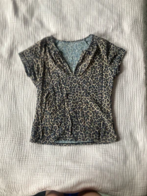 Leopardmönstrad v-ringad topp - Snygg topp med leopardmönster i beige och svart. Modellen har v-ringning och korta ärmar, perfekt för att ge outfiten lite edge. Tunt och mjukt material som sitter figurnära.