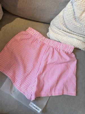 Nya i förpackning! Rosa och vita randiga shorts - Shorts i bomull med rosa och vita ränder, elastisk midja och knappar framtill. De har en loose passform och är perfekta för sommaren. Lätta och luftiga för en chill stil.