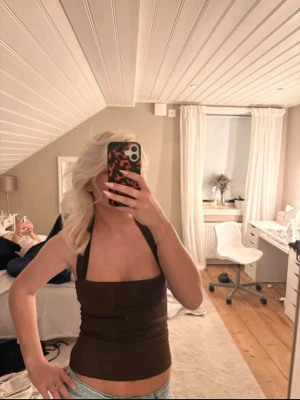Brun halterneck topp - Snygg brun halterneck topp med åtsittande passform och öppen rygg. Perfekt för dig som gillar en stilren och trendig look. Toppens material känns mjukt mot huden och den är ärmlös för en fräsch känsla.