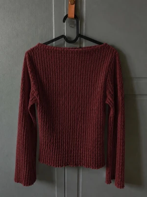 Vinröd långärmad tröja med struktur - Vinröd långärmad tröja med vågig struktur och lätt utsvängda ärmar. Tröjan har en rundad halsringning och är figurnära i modellen. Perfekt för dig som gillar en enkel men ändå unik look.