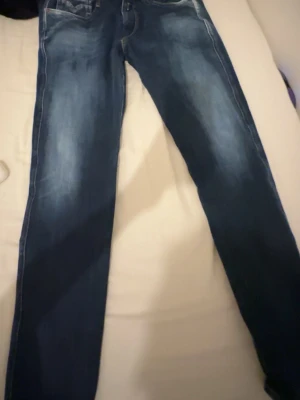 Mörkblå Replay jeans med slitningar - Säljer ett par mörkblå jeans från Replay med snygga slitningar och tvättade detaljer. Klassisk femficksmodell och smal passform. Perfekta för dig som gillar en stilren men ändå avslappnad look.