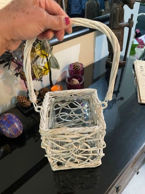 Vit korglykta med glasinsats - Säljer en fyrkantig vit korglykta med snirkligt flätad design och praktiskt handtag. Inuti finns en glasinsats som passar för värmeljus eller små ljus. Perfekt som dekorativ detalj i hemmet eller på balkongen.