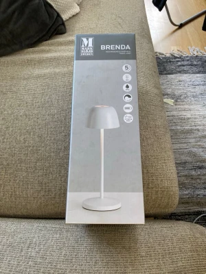 Vit bordslampa Markslöjd Brenda - Säljer en vit, uppladdningsbar bordslampa från Markslöjd, modell Brenda. Lampan har en stilren och minimalistisk design med rund fot och skärm. LED-belysning och laddas via medföljande laddningsbricka. Perfekt för skrivbord eller nattduksbord.