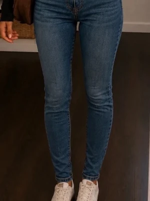 Blå skinny jeans med hög midja - Snygga blå skinny jeans med hög midja och klassisk femficksdesign. Jeansen har en smal passform hela vägen ner och är tillverkade i stretchigt denimtyg för extra komfort. Perfekta att matcha med sneakers eller boots.