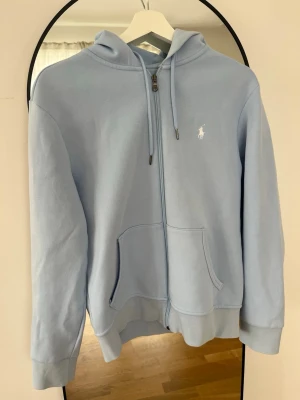 Ljusblå hoodie från Ralph Lauren - Ljusblå hoodie med dragkedja från Ralph Lauren. Nyköpt och använd en gång. 