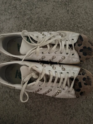 Adidas sneakers med nitar & leopardmönster - Unika vita Adidas sneakers med coola silverfärgade nitar längs sidorna och med  leopardmönster. Klassisk låg modell med snörning och grönt Adidas-tryck på plösen. 