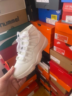 Vita Air Jordan 11 sneakers - Fräscha vita Air Jordan 11 sneakers med högt skaft och klassisk siluett. Skorna har en blandning av läder och syntetmaterial, med tydliga detaljer och tjock vit sula. Perfekta för dig som gillar streetwear och vill sticka ut med en ikonisk modell.