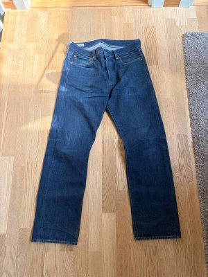 Mörkblå raka jeans från Levi's(32:32) - Säljer ett par klassiska mörkblå jeans från Levi's med rak passform och fem fickor. Jeansen har orangea sömmar och läderpatch bak i midjan. Perfekta för en clean och tidlös look.