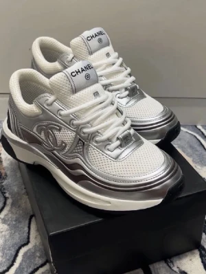 Chanel Runners - Snygga sneakers från Chanel i vitt och silver med ikoniska CC-loggan på sidan. Skorna har en chunky sula, mesh och läderdetaljer samt vita skosnören. Perfekta för dig som vill sticka ut med exklusiva och trendiga sneakers.