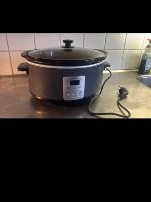 OBH Nordica slowcooker med digital display - En svart och silverfärgad slowcooker från OBH Nordica med digital display och kontrollpanel framtill. Grytan har glaslock och två handtag på sidorna. Perfekt för att laga grytor och långkok. Elsladd medföljer.