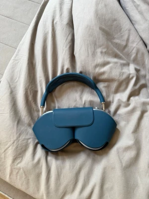 Apple AirPods Max blå over-ear hörlurar - Snygga Apple AirPods Max i blått med smart case. Over-ear design med mjuka öronkuddar och metallkåpor. Bygeln är vadderad för extra komfort och hörlurarna har en modern, stilren look. Perfekta för musik, gaming eller film.