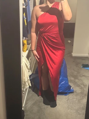 Röd balklänning - Snygg röd långklänning i oneshoulder-modell med slits framtill och dragkedja i sidan för att göra den enklare att ta på. Storlek 36 från Nelly och den är endast använd en gång. Den perfekta balklänningen!!!