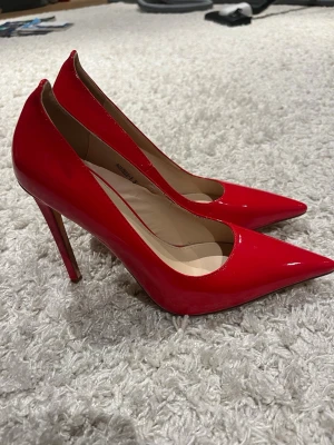 Röda lackpumps från Simmi - Säljer ett par snygga röda pumps från Simmi i glansigt lackmaterial. Skorna har spetsig tå och hög klack som ger en elegant siluett. Perfekta för dig som vill sticka ut med färg och stil. Klassisk modell som passar till många olika outfits.