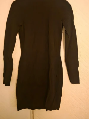 Svart ribbad klänning med öppen rygg - En svart ribbad klänning med öppen rygg och turtelneck. Från NAKD storlek M
