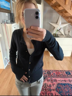 Svart kofta med guldknappar - Stilren svart kofta med långa ärmar och snygga guldknappar framtill. Modellen är figurnära och passar perfekt till jeans eller kjol. Koftan har ribbade muddar vid ärmslut och nederkant för en schysst passform.