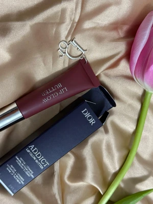 Dior Addict Lip Glow Butter Black Cherry - Dior Addict Lip Glow Butter i färgen Black Cherry 104. Läppbalsamet kommer i en elegant tub med silverdetaljer och en snygg Dior-logga. Färgen är en djup bärig vinröd ton och formulan är krämig och återfuktande. Perfekt för dig som vill ha både färg och vård till läpparna.