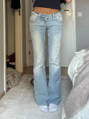 Ljusblå lågmidjade bootcut jeans Gina Tricot - Säljer ett par ljusblå lågmidjade bootcut jeans från Gina Tricot med hål på knä och lår. Jeansen har låg midja, klassiska fickor och är tillverkade i denim med en snygg tvätt. Perfekta för en trendig och avslappnad look. Endast använda 1-2 gånger! 💕💕