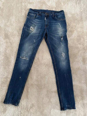 Classic Kenny Twist Jean - Säljer ett par blå skinny jeans med slitningar och hål på både fram- och baksida. Jeansen har klassisk femficksmodell, låg midja och coola detaljer som ger en trendig look. Perfekta för dig som gillar en avslappnad och edgy stil.
