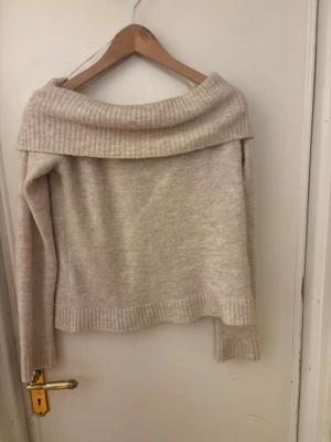 Beige off shoulder stickad tröja - Säljer en beige stickad off shoulder-tröja med bred krage och långa ärmar. Tröjan har ribbade muddar vid ärmslut och nederkant, och är gjord i ett mjukt material som passar perfekt för kyligare dagar.